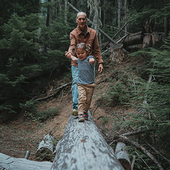 Man walking over log with grandson