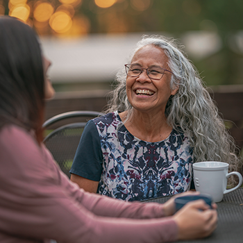 2 ladies laughing and chatting with cup of coffee